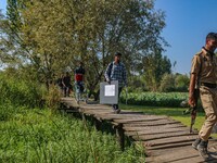 Polling officials, along with an Indian policeman, walk in the interiors of Dal Lake towards their designated polling station after collecti...