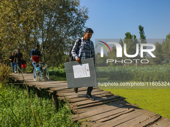 Polling officials walk in the interiors of Dal Lake towards their designated polling station after collecting election materials at a distri...