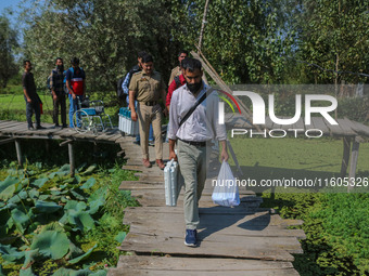 Polling officials along with Indian policemen walk in the interiors of Dal Lake towards their designated polling station after collecting el...