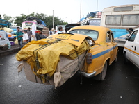 An overloaded yellow Ambassador taxi waits to unload consumer goods from its boot before loading a bus after arriving from a neighboring sta...