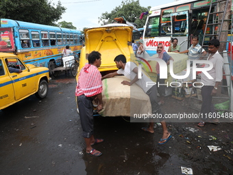 Labourers unload consumer goods from a yellow Ambassador taxi boot to load a bus after it arrives from a neighboring state at a bus terminal...