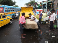 Labourers unload consumer goods from a yellow Ambassador taxi boot to load a bus after it arrives from a neighboring state at a bus terminal...