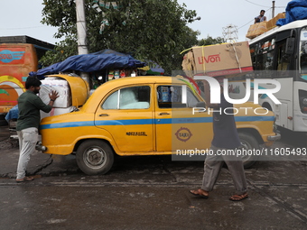 A person loads consumer goods onto a yellow Ambassador after unloading them from a bus that arrives from a neighboring state at a bus termin...