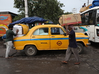 A person loads consumer goods onto a yellow Ambassador after unloading them from a bus that arrives from a neighboring state at a bus termin...