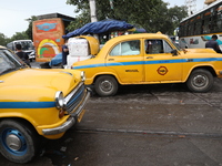 A unloads consumer goods from a yellow Ambassador taxi boot to load a bus after it arrives from a neighboring state at a bus terminal in Kol...