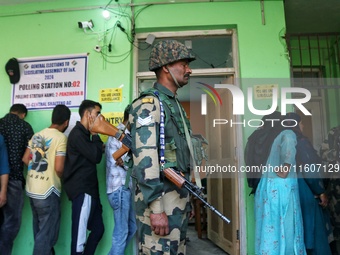 An Indian security personnel stands guard as voters queue to cast their ballots at a polling station during the second phase of assembly ele...