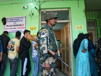 An Indian security personnel stands guard as voters queue to cast their ballots at a polling station during the second phase of assembly ele...