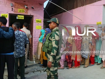 An Indian security personnel stands guard as voters queue to cast their ballots at a polling station during the second phase of assembly ele...