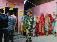 An Indian security personnel stands guard as voters queue to cast their ballots at a polling station during the second phase of assembly ele...