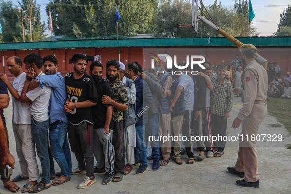 An Indian policeman stands guard as voters queue to cast their ballots at a polling station during the second phase of assembly elections in...