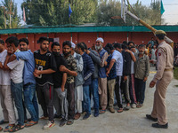 An Indian policeman stands guard as voters queue to cast their ballots at a polling station during the second phase of assembly elections in...