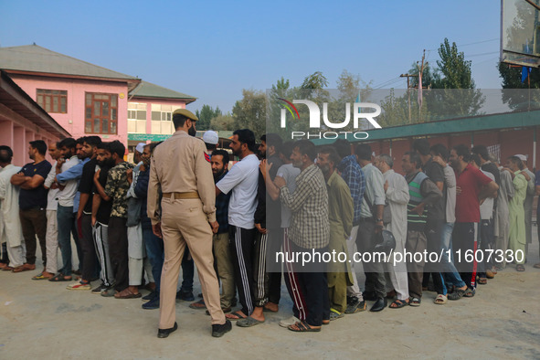 An Indian policeman stands guard as voters queue to cast their ballots at a polling station during the second phase of assembly elections in...