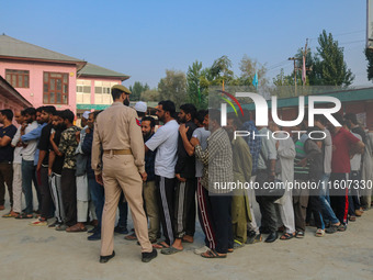 An Indian policeman stands guard as voters queue to cast their ballots at a polling station during the second phase of assembly elections in...