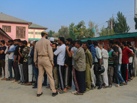 An Indian policeman stands guard as voters queue to cast their ballots at a polling station during the second phase of assembly elections in...