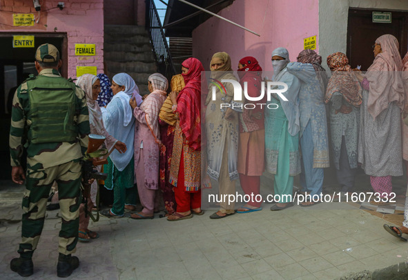 An Indian security personnel stands guard as women voters queue to cast their ballots at a polling station during the second phase of assemb...