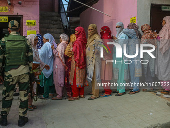 An Indian security personnel stands guard as women voters queue to cast their ballots at a polling station during the second phase of assemb...