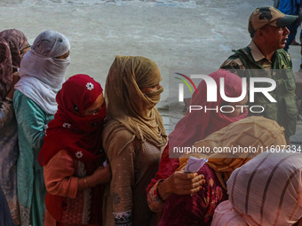 An Indian security personnel stands guard as women voters queue to cast their ballots at a polling station during the second phase of assemb...