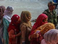 An Indian security personnel stands guard as women voters queue to cast their ballots at a polling station during the second phase of assemb...