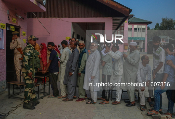 An Indian security personnel stands guard as voters queue to cast their ballots at a polling station during the second phase of assembly ele...