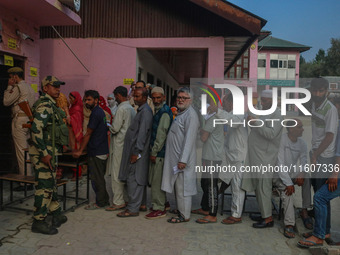 An Indian security personnel stands guard as voters queue to cast their ballots at a polling station during the second phase of assembly ele...