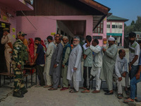 An Indian security personnel stands guard as voters queue to cast their ballots at a polling station during the second phase of assembly ele...