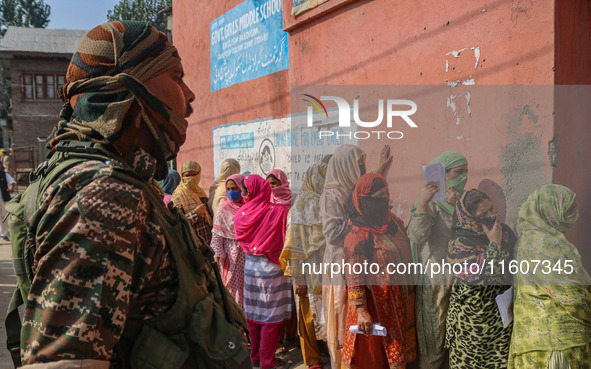 An Indian security personnel stands guard as women voters queue to cast their ballots at a polling station during the second phase of assemb...