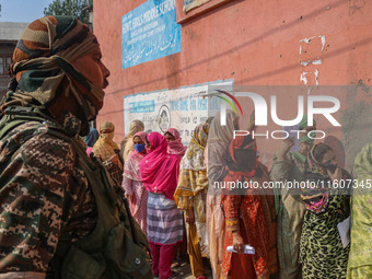 An Indian security personnel stands guard as women voters queue to cast their ballots at a polling station during the second phase of assemb...