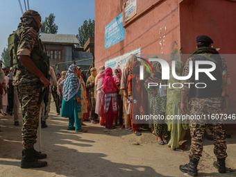 Indian security personnel stand guard as women voters queue to cast their ballots at a polling station during the second phase of assembly e...