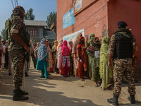 Indian security personnel stand guard as women voters queue to cast their ballots at a polling station during the second phase of assembly e...