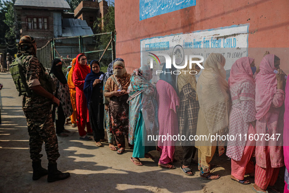 An Indian security personnel stands guard as women voters queue to cast their ballots at a polling station during the second phase of assemb...