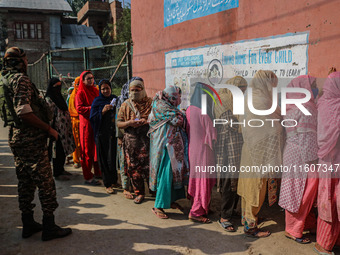 An Indian security personnel stands guard as women voters queue to cast their ballots at a polling station during the second phase of assemb...