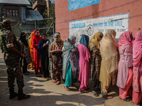 An Indian security personnel stands guard as women voters queue to cast their ballots at a polling station during the second phase of assemb...