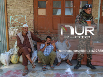 An Indian security personnel stands guard as people show their ink-marked fingers after casting their ballots at a polling station during th...