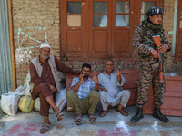 An Indian security personnel stands guard as people show their ink-marked fingers after casting their ballots at a polling station during th...