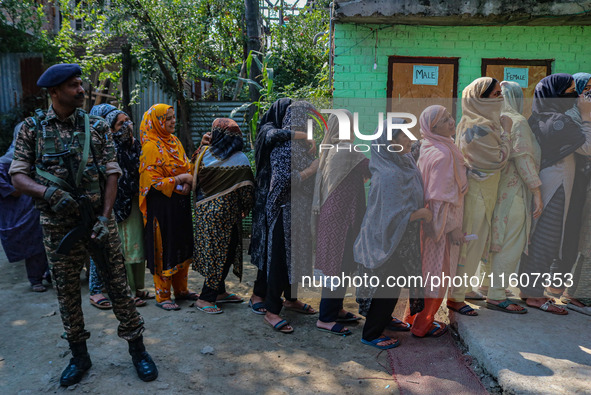 An Indian security personnel stands guard as women voters queue to cast their ballots at a polling station during the second phase of assemb...