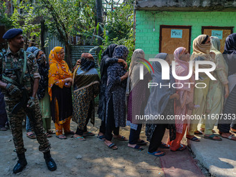 An Indian security personnel stands guard as women voters queue to cast their ballots at a polling station during the second phase of assemb...