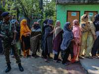 An Indian security personnel stands guard as women voters queue to cast their ballots at a polling station during the second phase of assemb...