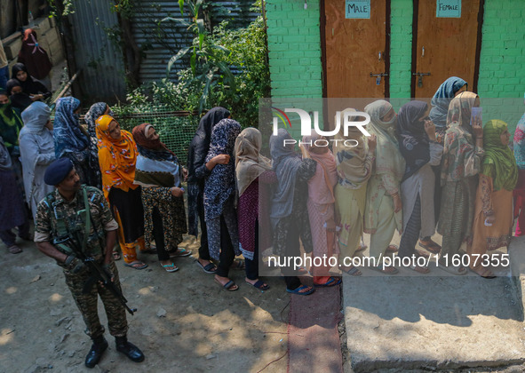 An Indian security personnel stands guard as women voters queue to cast their ballots at a polling station during the second phase of assemb...