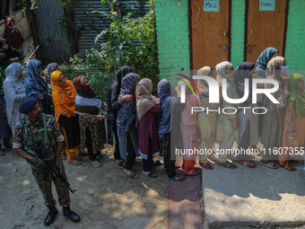 An Indian security personnel stands guard as women voters queue to cast their ballots at a polling station during the second phase of assemb...