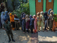 An Indian security personnel stands guard as women voters queue to cast their ballots at a polling station during the second phase of assemb...