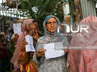 People display their voting cards as they wait in line to cast their votes at a polling station during the second phase of assembly election...