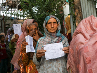 People display their voting cards as they wait in line to cast their votes at a polling station during the second phase of assembly election...