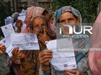 People display their voting cards as they wait in line to cast their votes at a polling station during the second phase of assembly election...