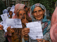 People display their voting cards as they wait in line to cast their votes at a polling station during the second phase of assembly election...