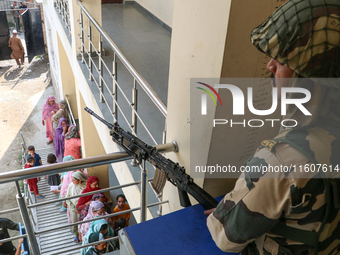 Indian paramilitary troopers stand alert as people wait in line to cast their votes at a polling station during the second phase of assembly...