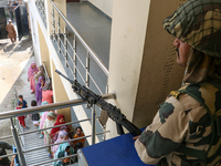 Indian paramilitary troopers stand alert as people wait in line to cast their votes at a polling station during the second phase of assembly...