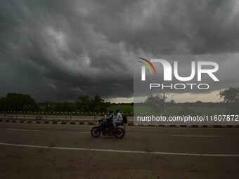 A man rides a bike as dark clouds loom over the sky in Morigaon District of Assam, India, on September 25, 2024. (