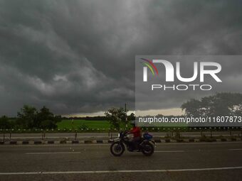 A man rides a bike as dark clouds loom over the sky in Morigaon District of Assam, India, on September 25, 2024. (