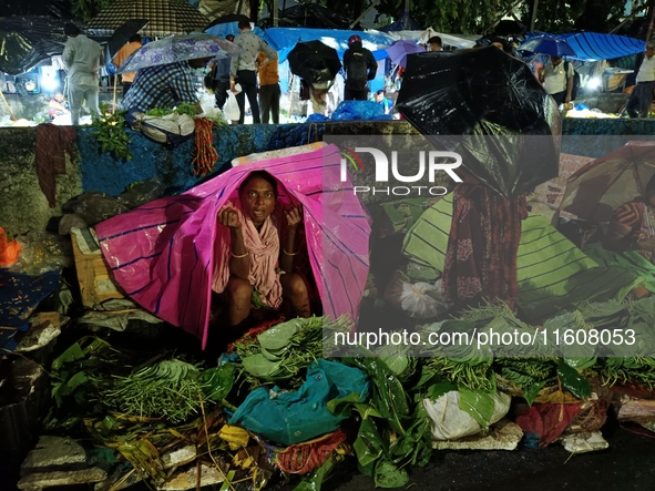 A woman covers her stall with a plastic sheet and waits for customers during rainfall in Kolkata, India, on September 25, 2024. 