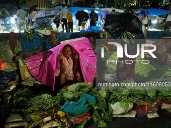 A woman covers her stall with a plastic sheet and waits for customers during rainfall in Kolkata, India, on September 25, 2024. (